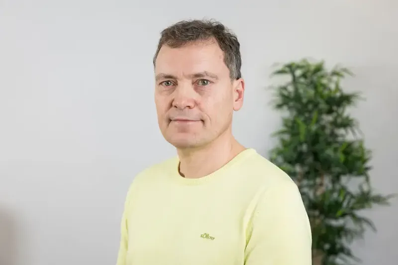 Volkmar Roß trägt einen hellgelben Pullover und blickt ruhig in die Kamera.