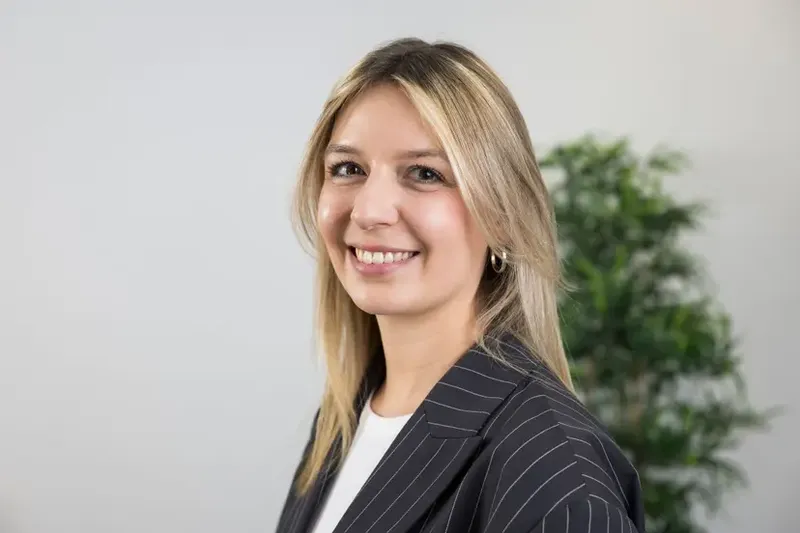 Paula Schmidt mit blondem Haar und Nadelstreifenblazer lächelt in die Kamera.