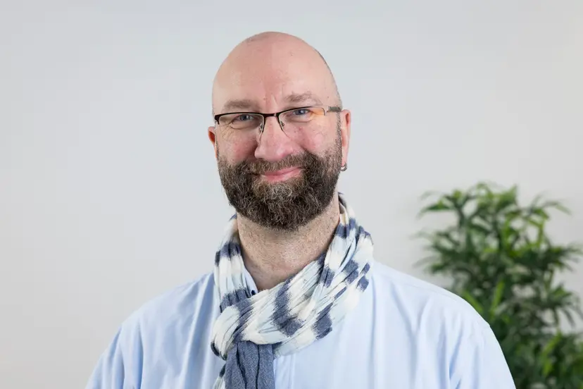 Sascha Böge mit Brille, Bart und gestreiftem Schal lächelt in die Kamera.
