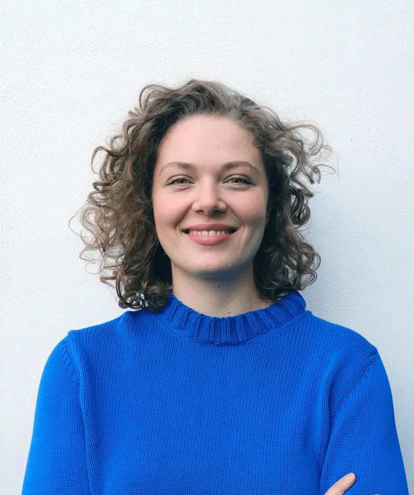 Elisabeth Kraus mit lockigem Haar und blauem Pullover lächelt in die Kamera.